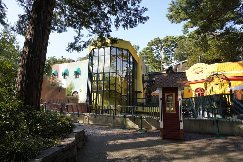 A yellow building with a glass facade, surrounded by trees and a stone wall.