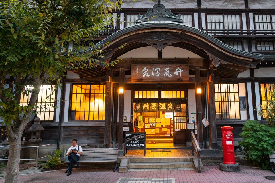 A traditional Japanese building with a wooden facade, a sign with Japanese characters, and a red post box.