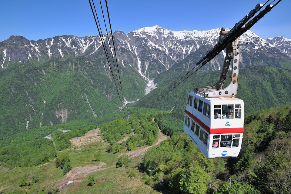 A cable car in a mountainous area with snow-capped peaks and lush green valleys.