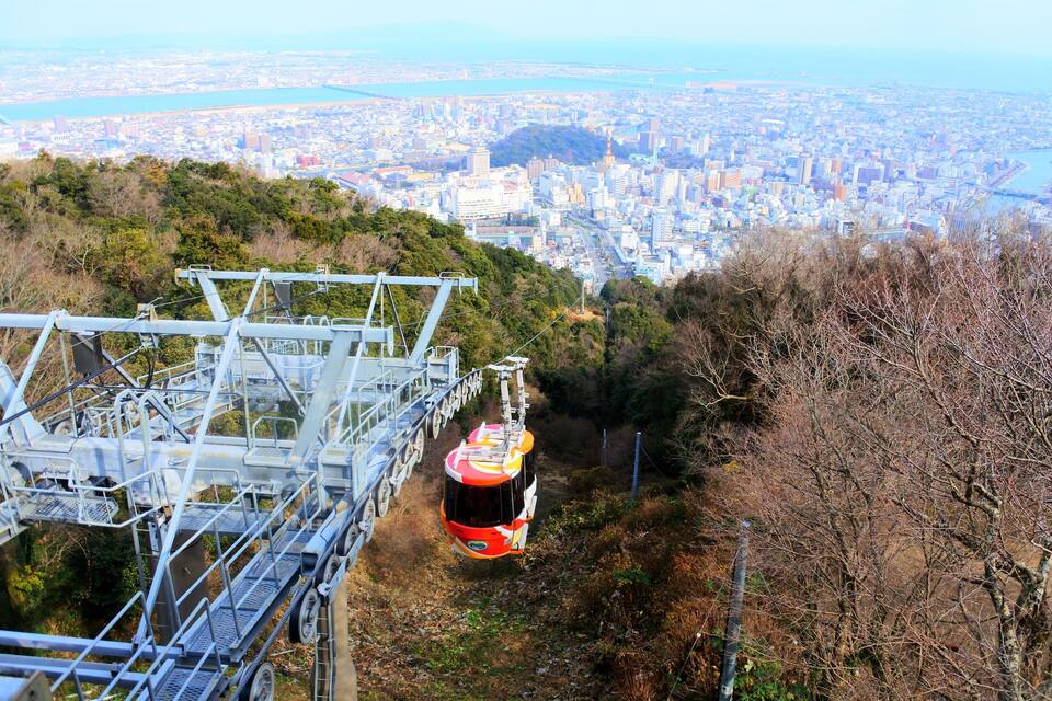 Um teleférico movendo-se ao longo de uma trilha de montanha, com um horizonte urbano ao fundo.