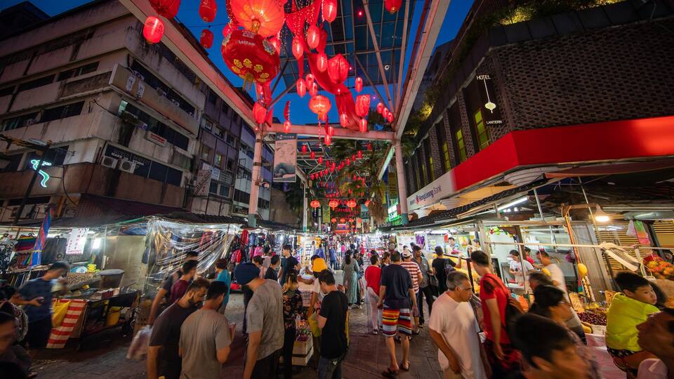 Un mercado callejero animado en la noche, con faroles rojos colgando sobre él.