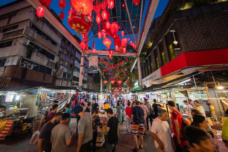 A bustling street market at night with red lanterns hanging overhead.