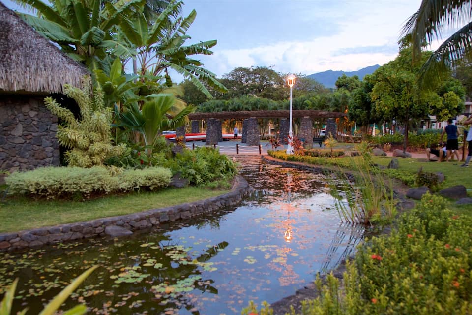 Um jardim com lago, muros de pedra e plantas tropicais.