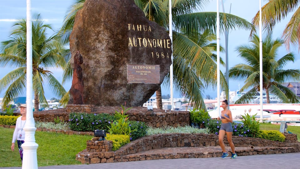 A large rock with inscriptions and a plaque, surrounded by greenery and palm trees.