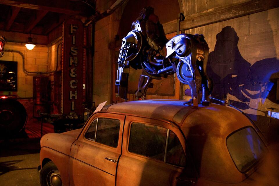 Um carro antigo com um robô em cima, em uma garagem mal iluminada com uma placa escrita 'FISHCH'.