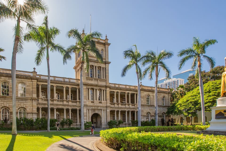 A historic building with classical architecture, palm trees, and a statue.