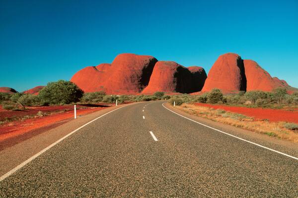 A road leading to red rock formations under a clear blue sky.