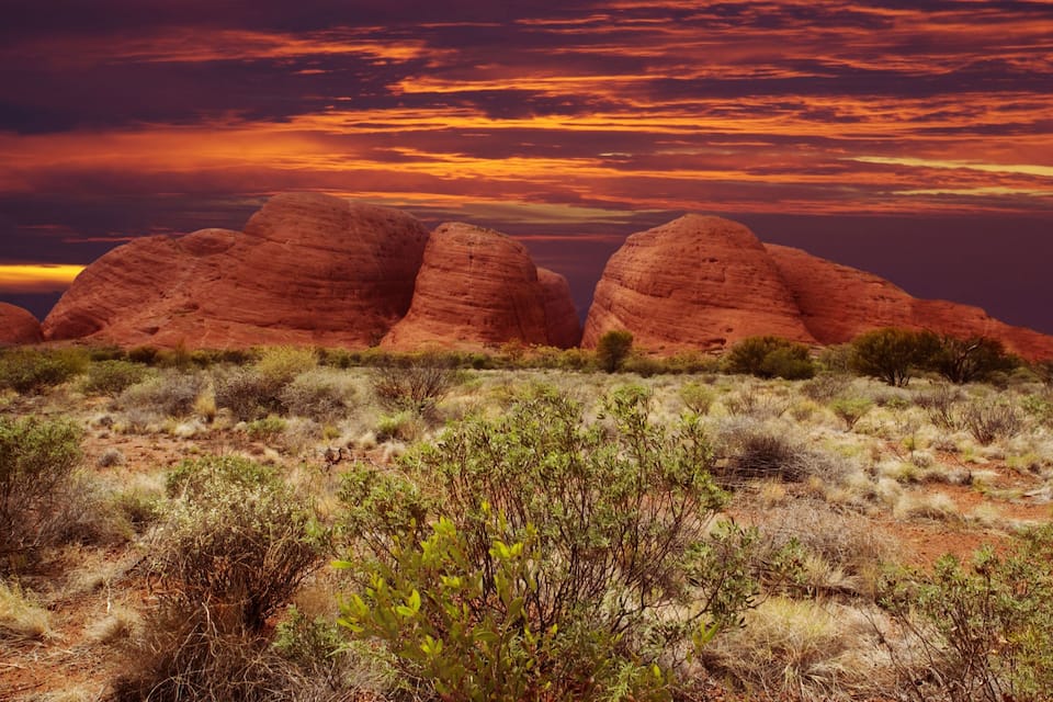 A desert landscape with red rock formations and sparse vegetation under a colorful sunset sky.