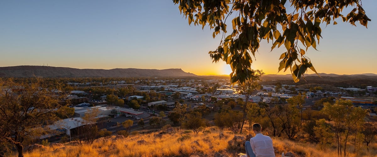 A person sitting on a rock overlooking a town at sunset.