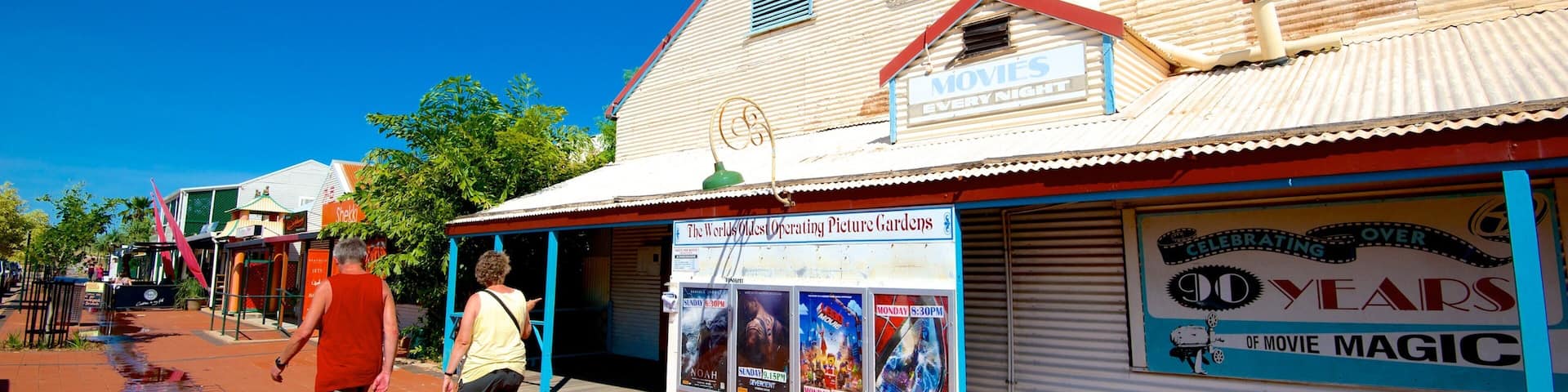A vintage movie theater with a sign reading "The World's Oldest Operating Picture Gardens" and a poster advertising "Celebrating 100 Years of Movie Magic."