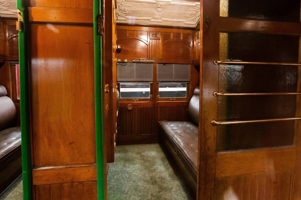 Interior de um trem antigo com painéis de madeira, placa indicando que não é área para fumantes e um banco.