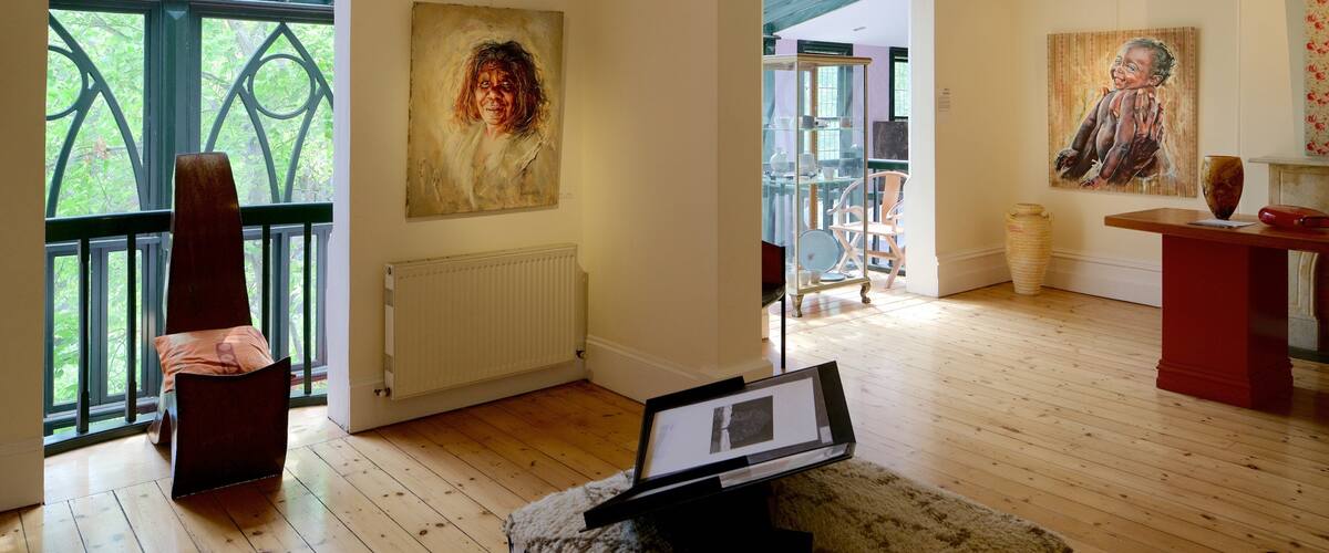 An art gallery with wooden floors, a large painting on the wall, and a sculpture on a pedestal.