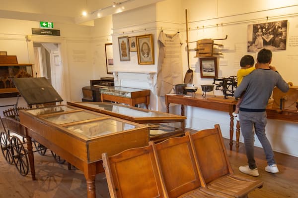 Une exposition de musée présentant des objets historiques, notamment un chariot en bois et une vitrine contenant divers articles.