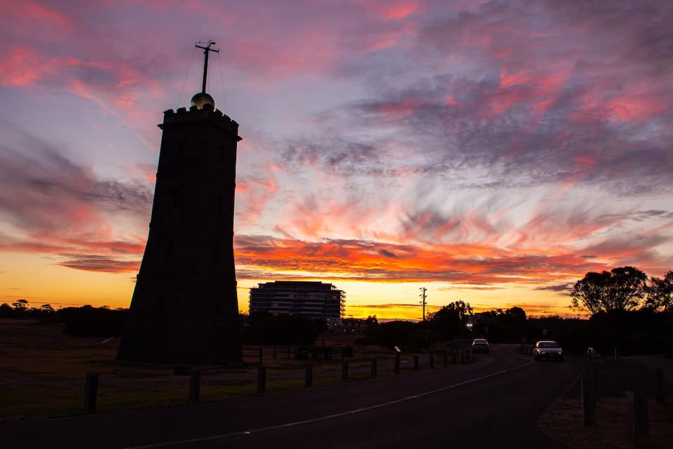 Ein hohes Monument mit einem Kreuz an der Spitze, vor einem leuchtenden Abendhimmel.
