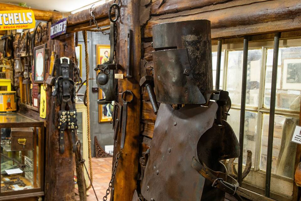 En rustik butik med antikke værktøjer og udstyr, herunder en stor metalpresse og et skilt med teksten "MITCHELLS THE BRUSH PEOPLE".
