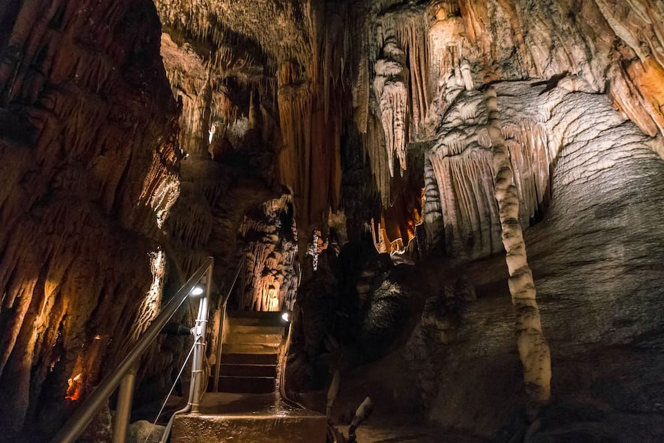 A cave with stalactites and stalagmites, a staircase, and a light source.