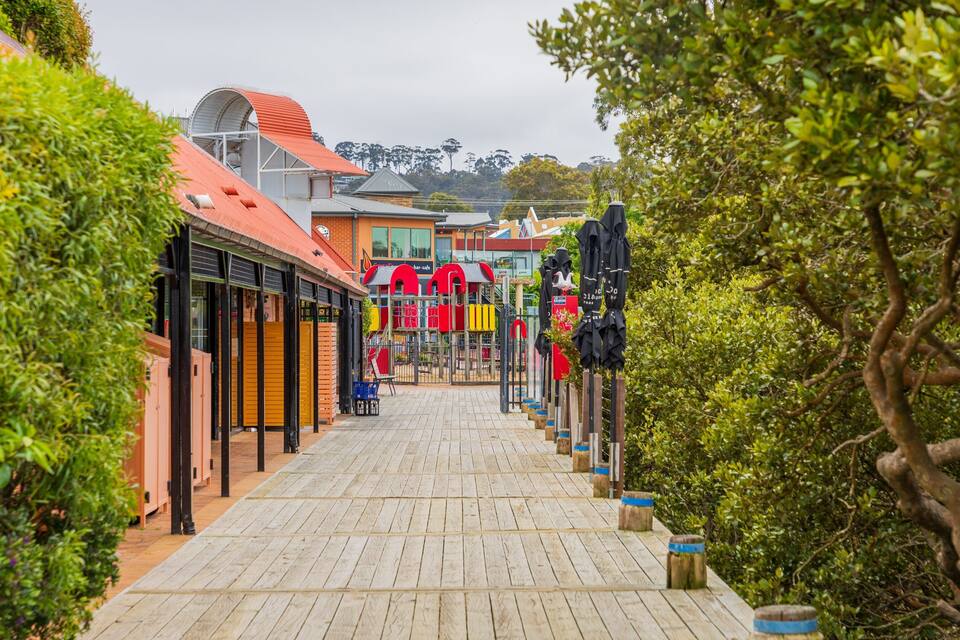 A wooden boardwalk leading to a colorful playground with a cafe in the background.
