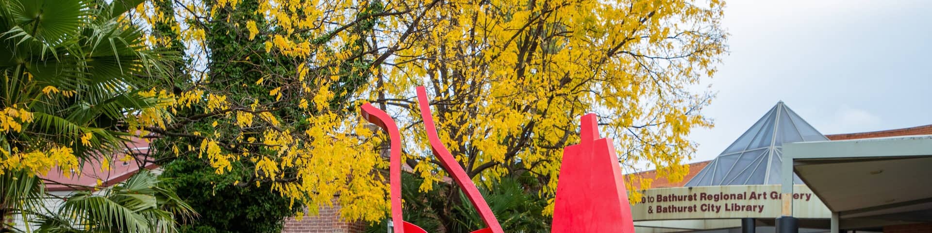 A red abstract sculpture in a park with a building labeled "Bathurst Regional Art Gallery & Bathurst City Library" in the background.