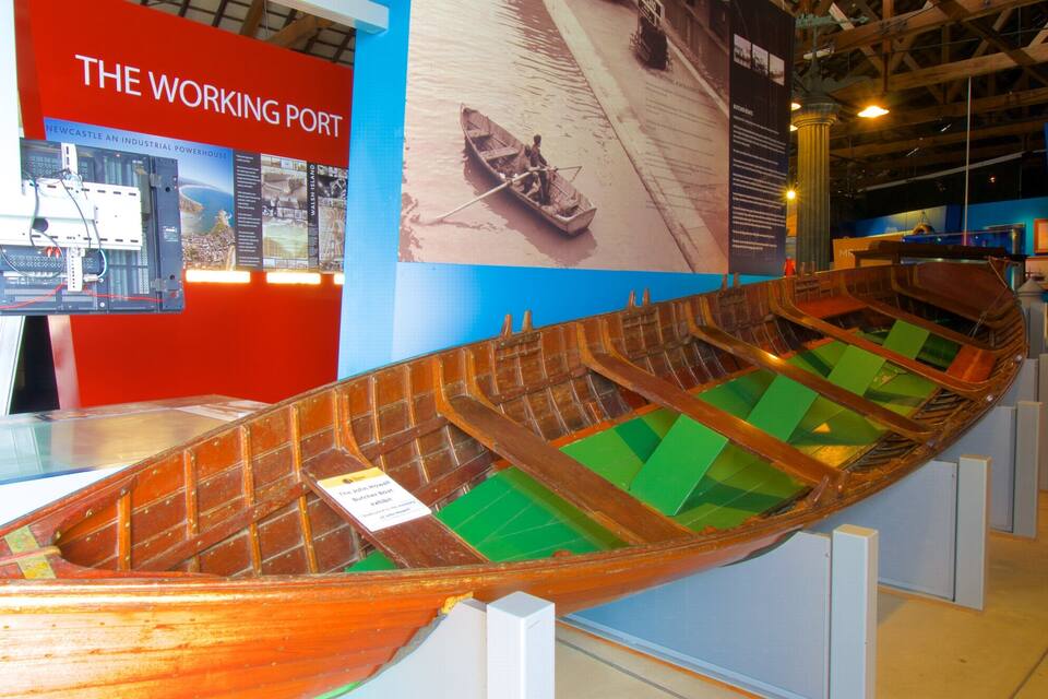 A wooden boat model in a museum display with informational signs in the background.
