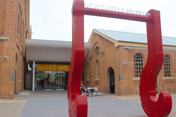 The entrance to the Newcastle Museum with a prominent red archway and a brick building in the background.
