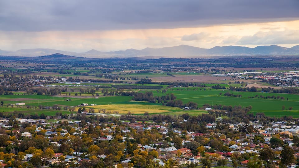 A rural landscape with a town, green fields, and mountains in the background.