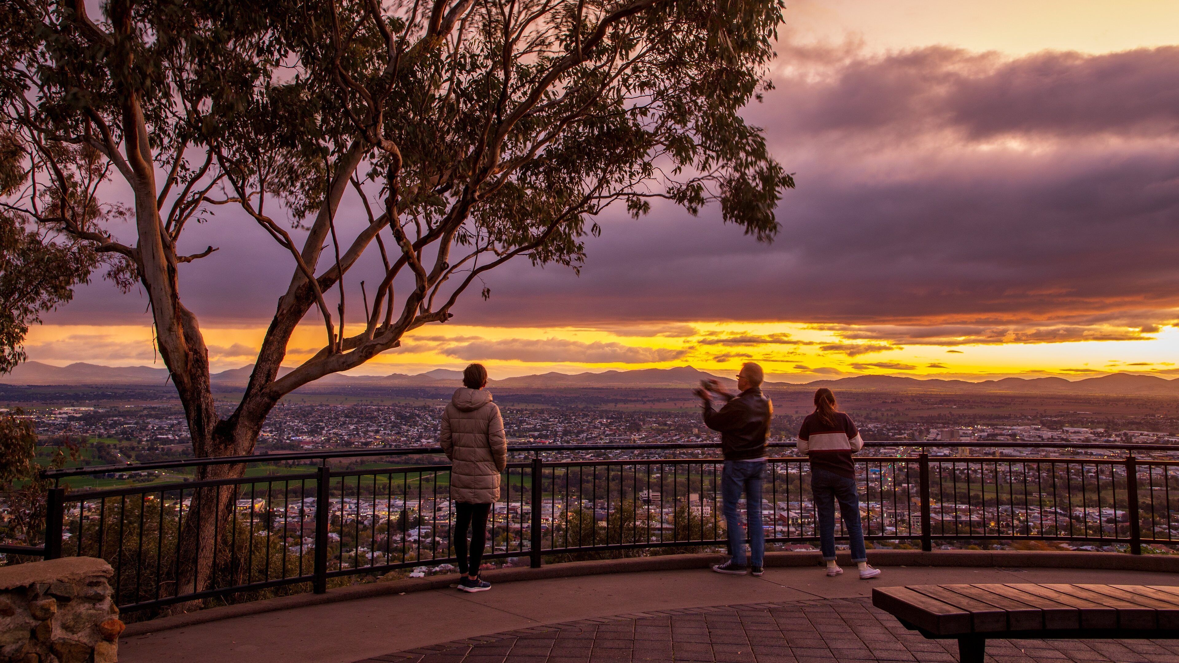 A sunset view from a park bench overlooking a cityscape.