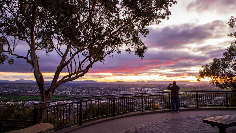 A person standing on a park bench overlooking a cityscape at sunset.