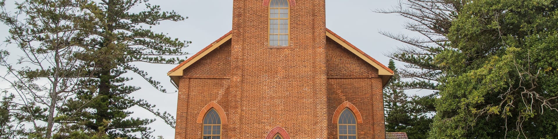 A brick church with a clock tower, arched windows, and a cross on top.