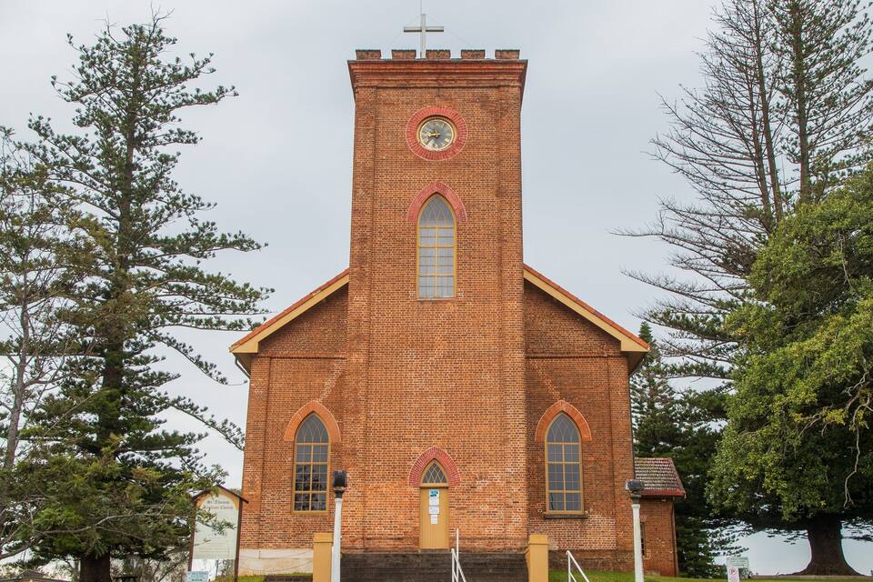 A brick church with a clock tower, arched windows, and a cross on top.