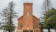 Une église en briques dotée d’un clocher, de fenêtres en arc de cercle et d’une croix au sommet.