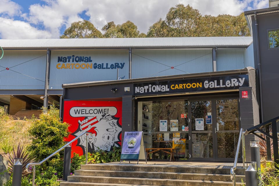 The entrance to the National Cartoon Gallery with a 'Welcome!' sign and a 'Behind the Lines' poster.