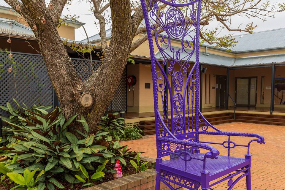 A purple wrought iron chair in a courtyard with a tree and plants.