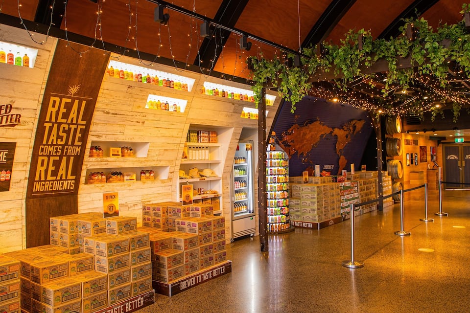 Exhibición de una cervecería con estantes de madera, una sección refrigerada y pilas de cajas de cerveza.