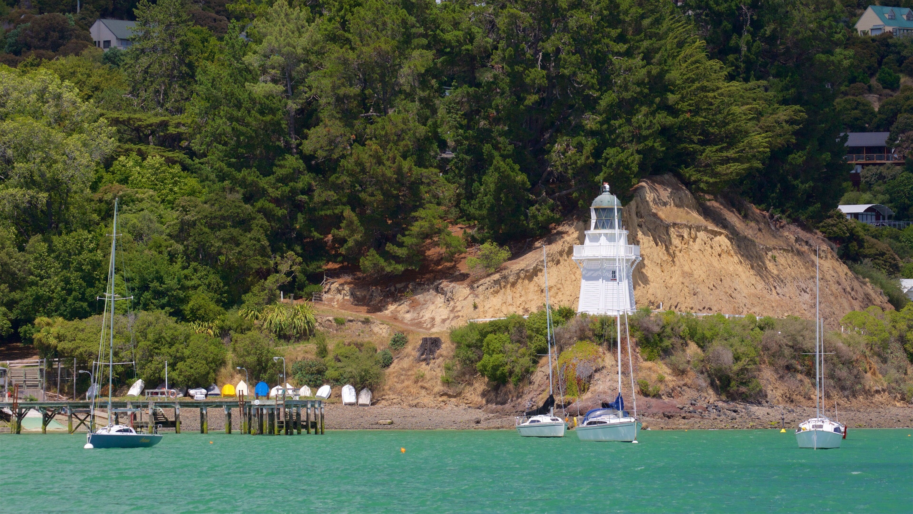 A coastal scene with a lighthouse, boats, and a pier.
