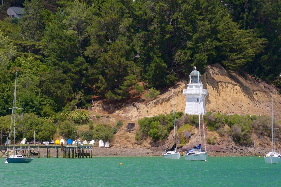 A coastal scene with a lighthouse, boats, and a pier.