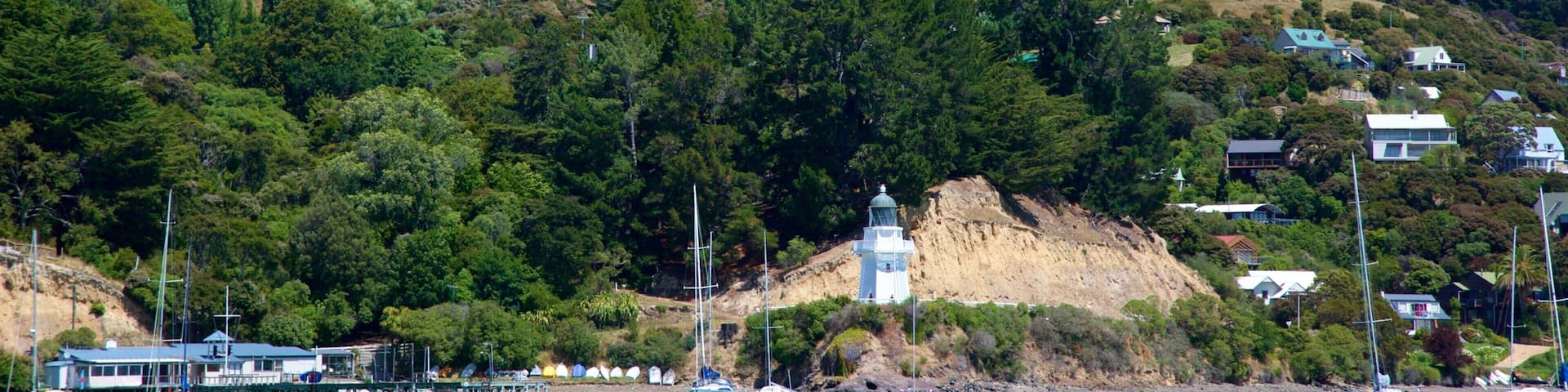 A coastal landscape with a lighthouse, boats, and houses on a hillside.