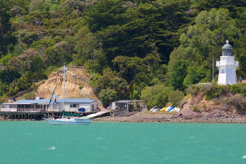 A coastal scene with a lighthouse, a boat, and a building on a hillside.