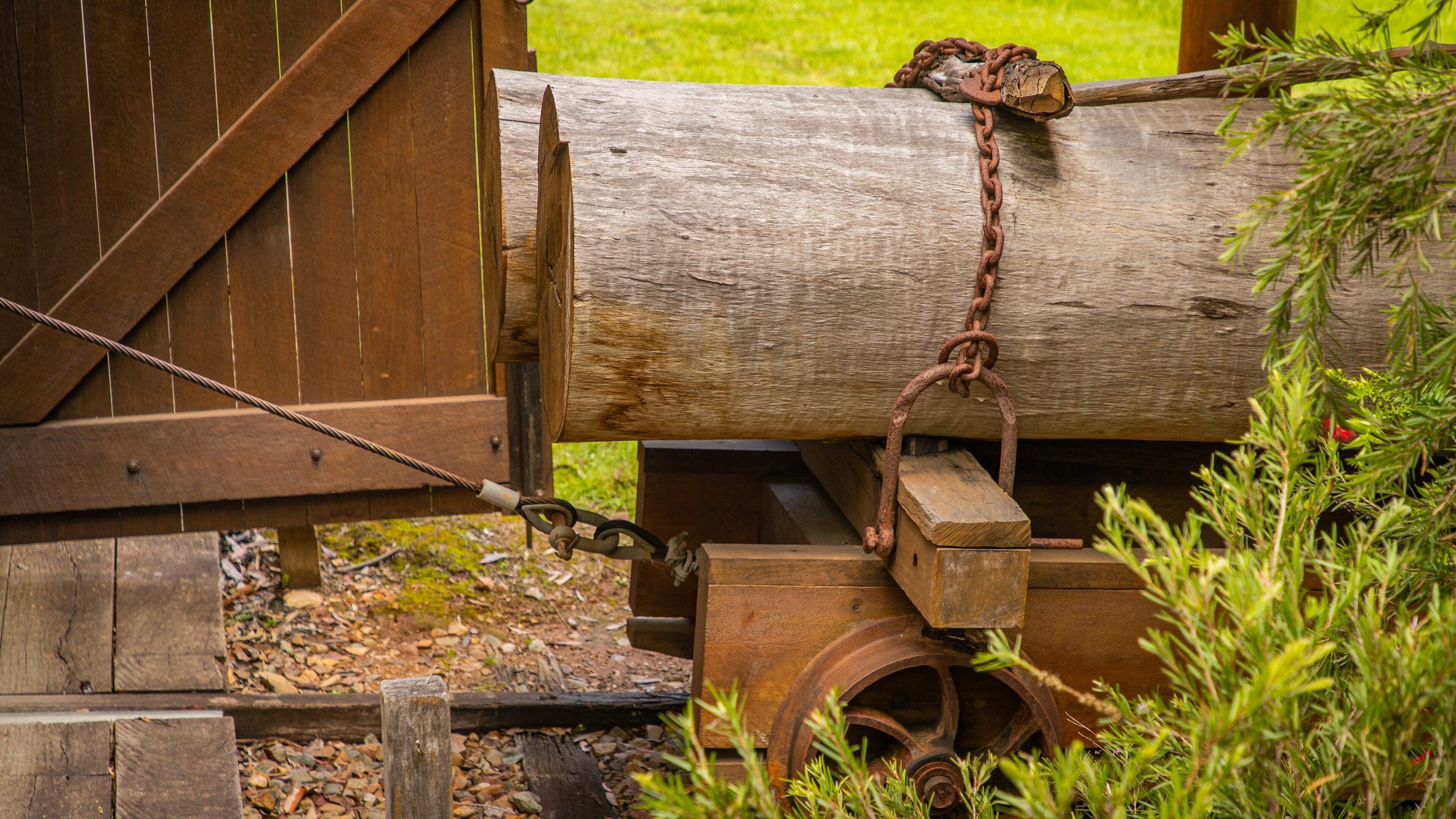Een houten constructie met een grote boomstam, een roestige ketting en een wielmechanisme.