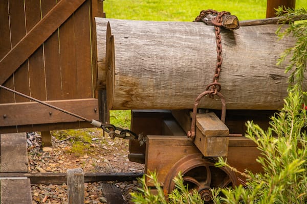 Une structure en bois comprenant un gros tronc d’arbre, une chaîne rouillée et un mécanisme à roue.
