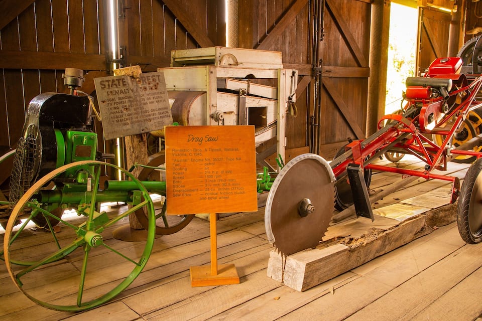 A vintage tractor with a green front wheel and a red rear wheel, a wooden signboard, and a red tractor with a large flywheel.