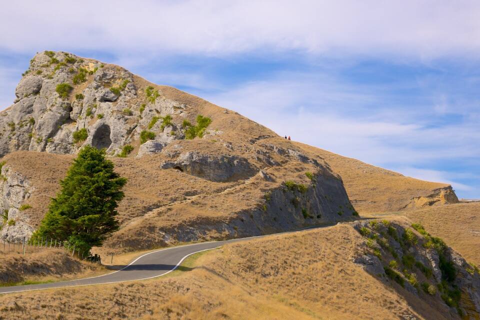 Una strada tortuosa su un paesaggio collinare e secco, con vegetazione rada e cielo sereno.