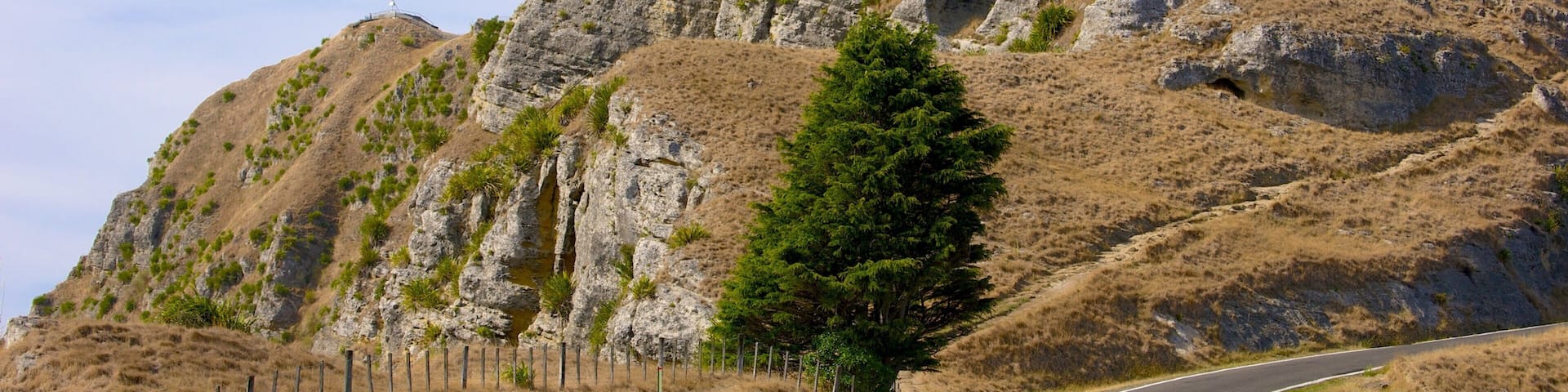 A winding road leading to a rocky hill with sparse vegetation and a clear sky.