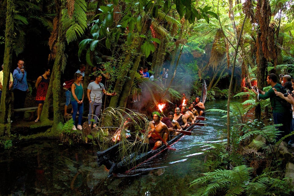 A group of people observing a ritual in a lush, green forest with a river.