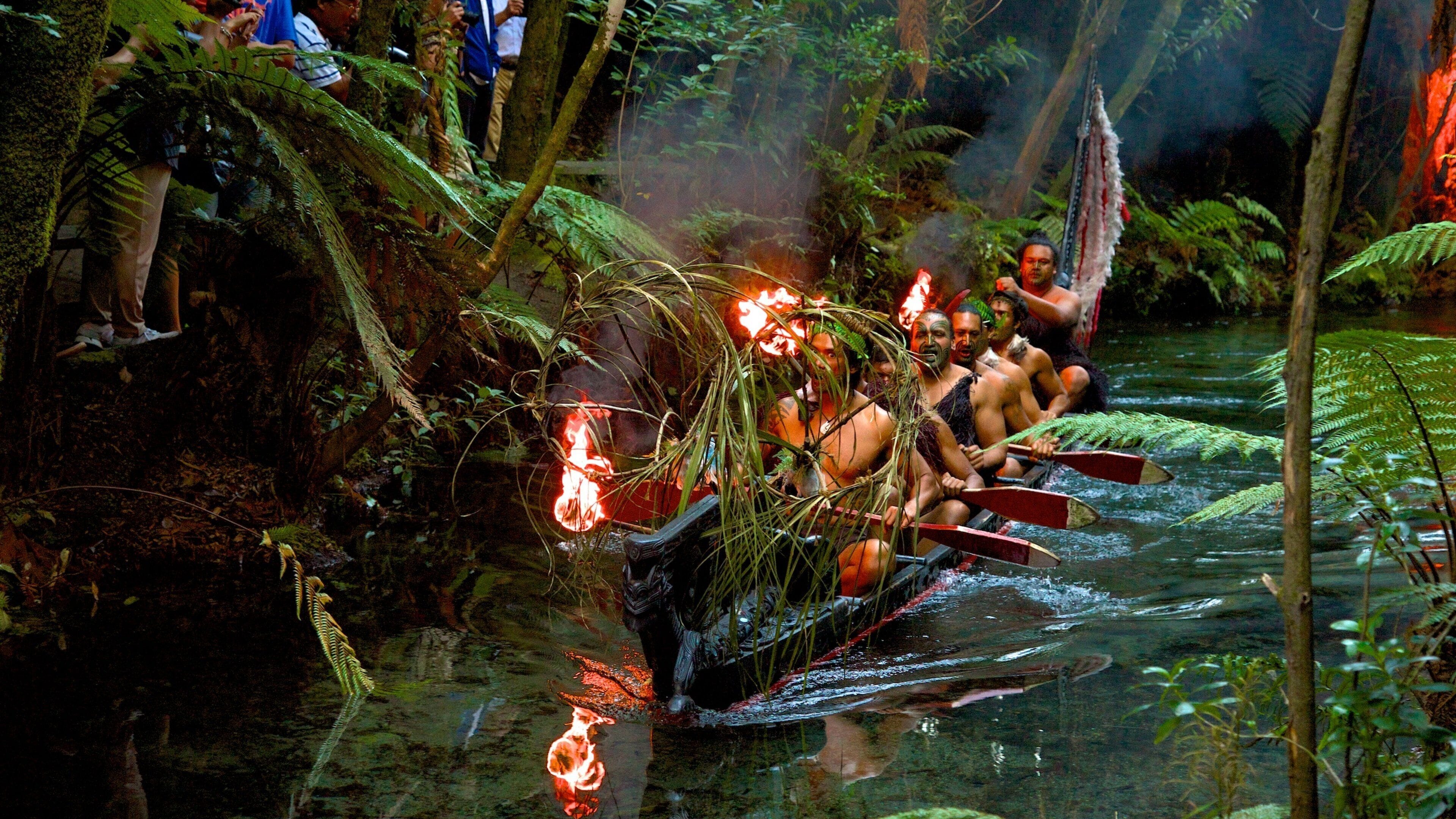 A canoe with people paddling through a river surrounded by dense greenery.