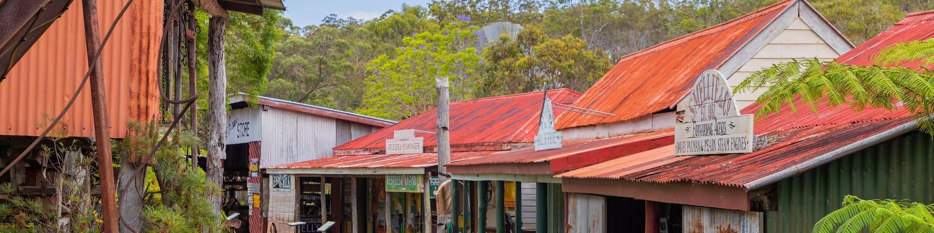 A rural street with old buildings, a sign for a store, and a dirt path.