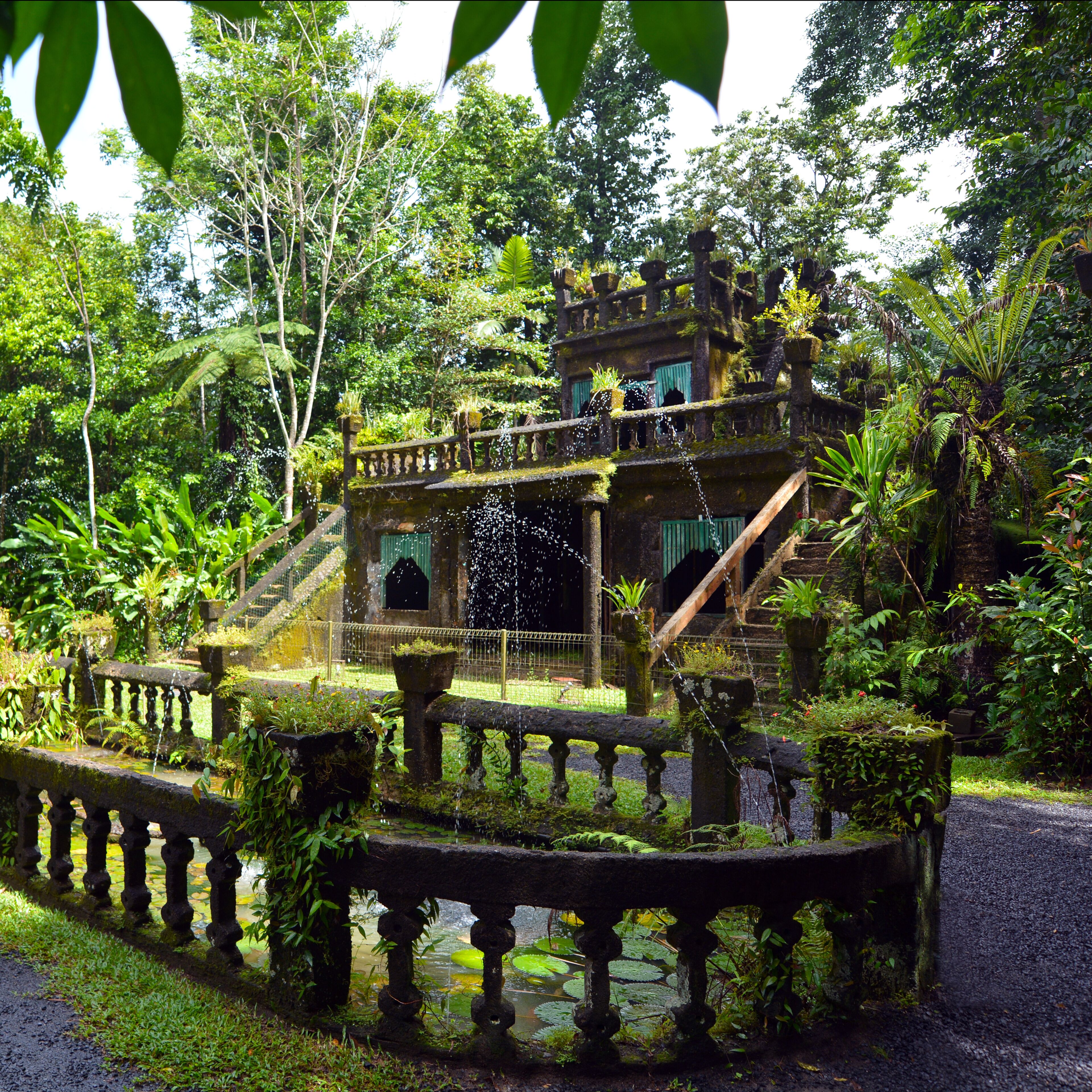 Un exuberante jardín con un puente de piedra, una fuente y una estructura de varios niveles rodeada de follaje denso.