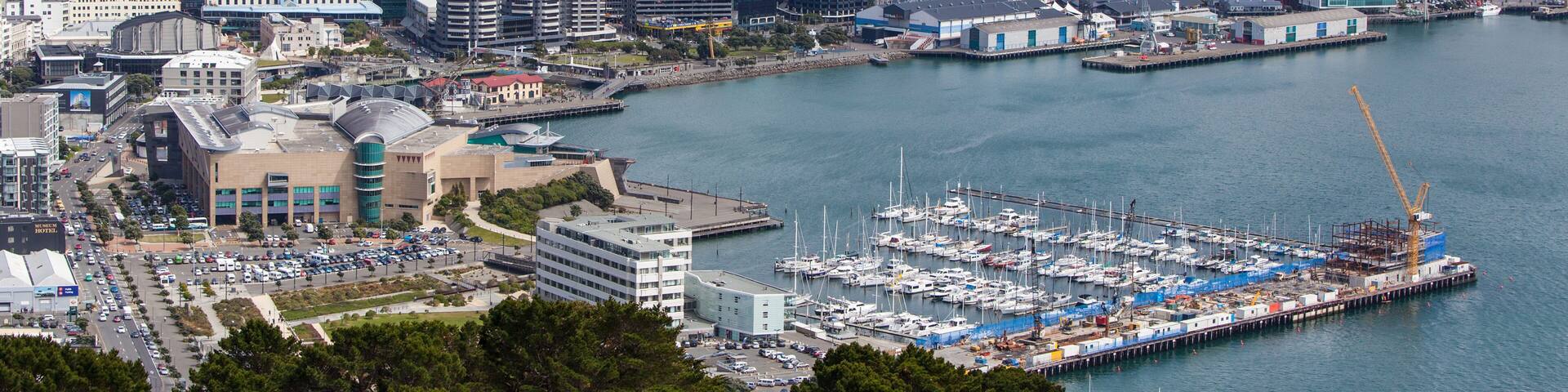 Un paisaje urbano costero con un puerto deportivo, edificios modernos y montañas al fondo.