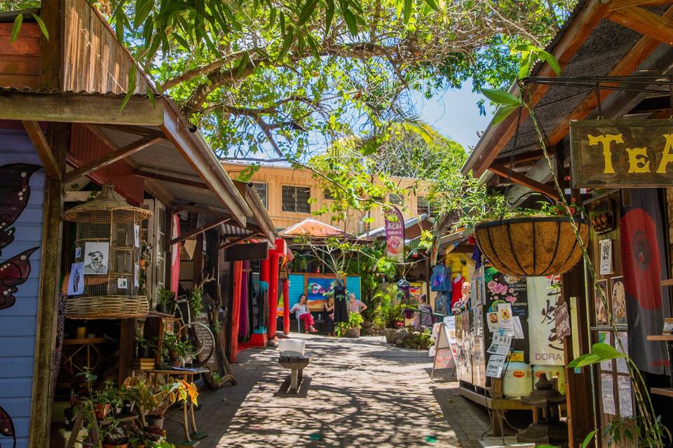 A narrow street with wooden buildings, a sign reading "TEA", and various shops and stalls.