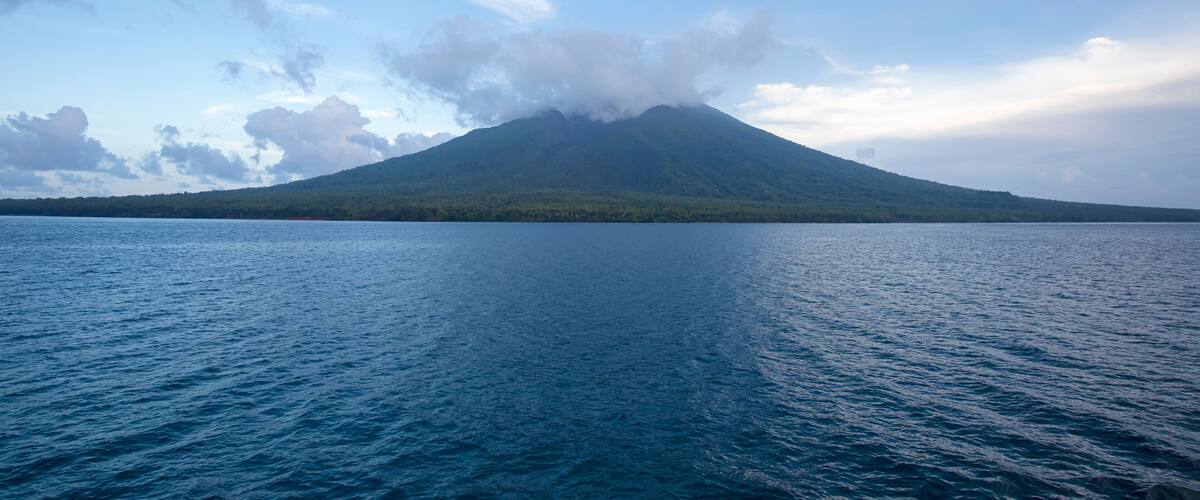 A volcano surrounded by a calm lake and a clear sky.