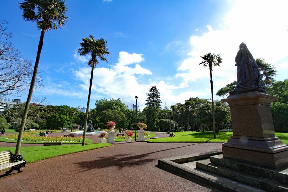 A park with a statue, palm trees, and flower beds.